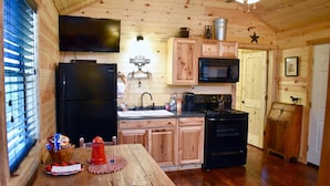 Interior de una cabaña de madera con cocina que incluye un refrigerador negro, microondas y estufa.