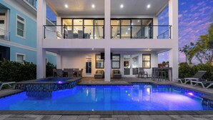 Ein modernes, zweistöckiges Haus mit Swimmingpool, Sitzgelegenheiten im Freien und einem Balkon.