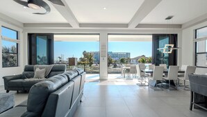 Ein modernes Wohnzimmer mit einer Couch, einem Esstisch und Stühlen, große Fenster mit Blick auf Gebäude und Palmen.
