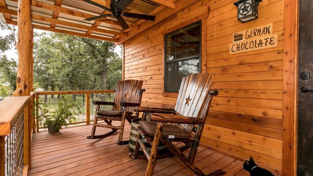 Une cabane en bois avec une véranda, deux fauteuils à bascule, une table et une pancarte indiquant « Chocolat allemand ».
