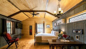 Une pièce chaleureuse dans un chalet en rondins, avec un lit, un fauteuil rouge, une table en bois et un ventilateur de plafond.