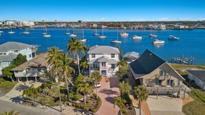 A coastal property with a marina, featuring multiple boats, a large house with a balcony, and a well-maintained garden with palm trees. - Bay Front with Private Pool - North Island - 3BR Dock Holiday (Fort Myers Beach)