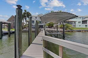 A waterfront walkway with a covered seating area, wooden posts, and a water body. - Bay Front with Private Pool - North Island - 3BR Dock Holiday (Fort Myers Beach)