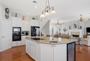 Une cuisine spacieuse avec des meubles blancs, un comptoir en granit et un îlot central. On y trouve également un coin repas avec une cheminée et un ventilateur de plafond.