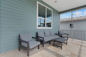 Ein Balkon mit einer grauen Couch und zwei Sesseln, einem kleinen Tisch und einem Fenster mit Blick zum Himmel.