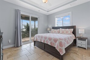 A bedroom with a large bed, a nightstand, a lamp, and a view of the outdoors through a sliding glass door. - Grande Palermo – Come stay and experience coastal living at its best! (Fort Myers Beach)
