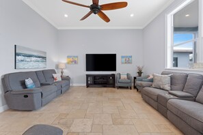 A living room with a ceiling fan, a flat-screen TV, and artwork on the walls. - Grande Palermo – Come stay and experience coastal living at its best! (Fort Myers Beach)