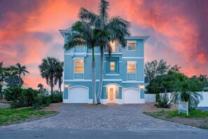 A two-story house with a blue exterior and white trim, a driveway leading to the front door, and a palm tree in front. - Grande Palermo – Come stay and experience coastal living at its best! (Fort Myers Beach)