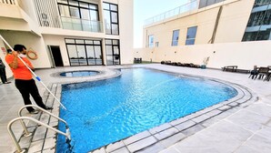 Una piscina con alguien limpiándola, rodeada por un edificio moderno con ventanas grandes y suelo de baldosas.