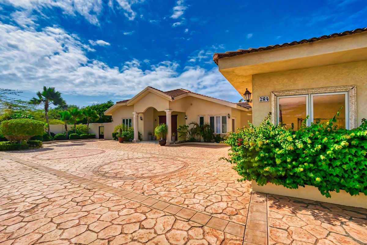 A house with a stone patio, a number 284 sign, and lush greenery.