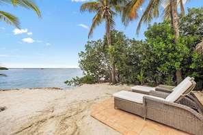 A beach with wicker lounge chairs and a view of the ocean.
