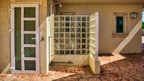 A building with a stone-tiled patio, a white door, and a window with a decorative frame.