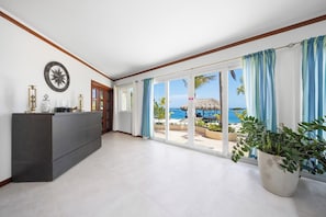 A spacious room with a large sliding glass door leading to a balcony with a view of the ocean and palm trees.