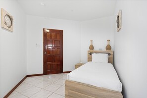 A bedroom with a wooden door, a bed with a headboard, and two wall-mounted vases.