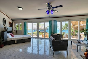 A room with a bed, a sofa, a dining table, and a ceiling fan.