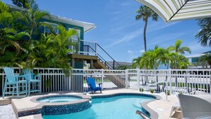 A swimming pool with a tiled edge, surrounded by a white fence, blue chairs, and a palm tree.