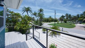 A wooden deck with a metal railing overlooking a street lined with palm trees and a clear blue sky.
