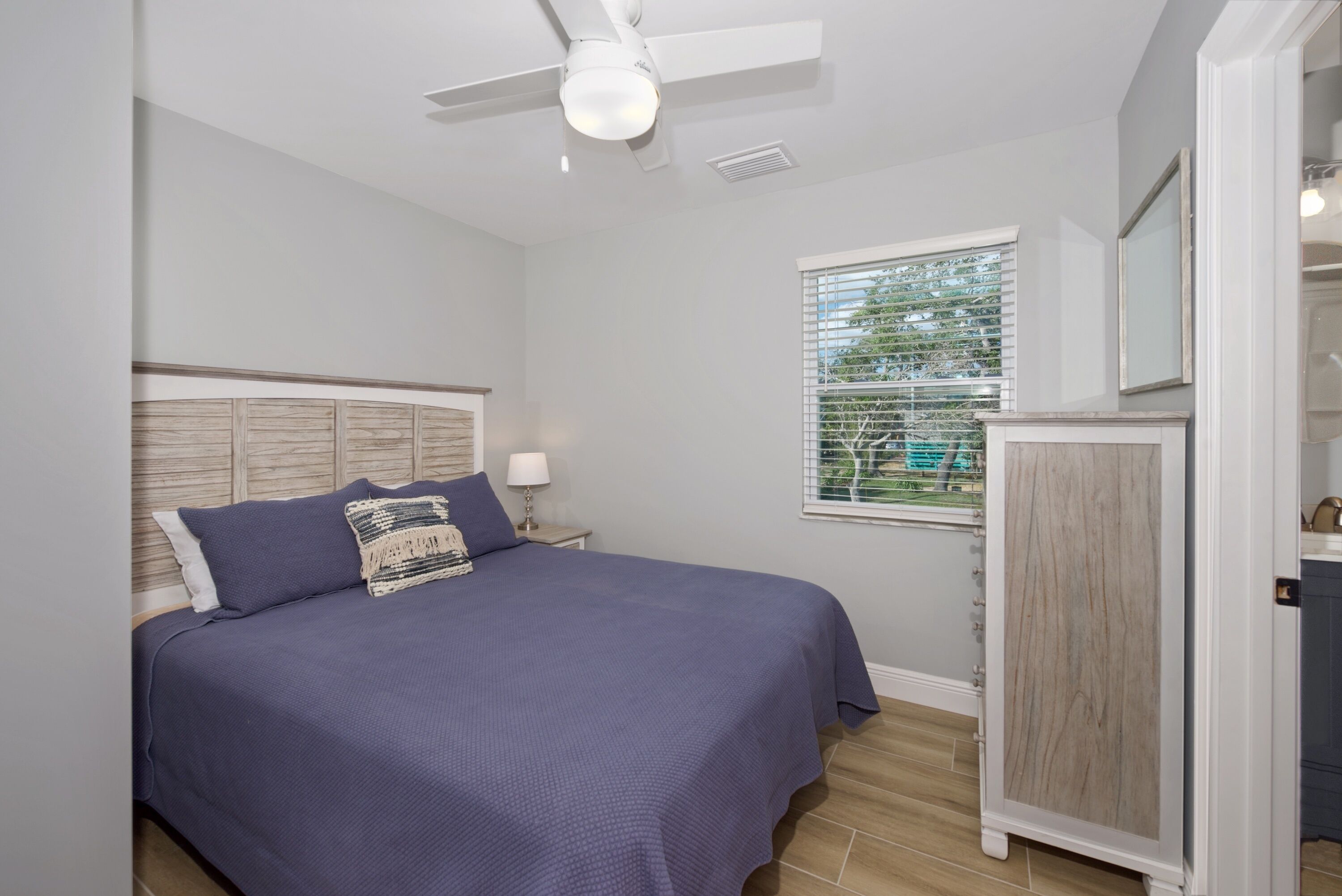 Un dormitorio con cama, ventilador de techo, ventana con persianas y un armario de madera.