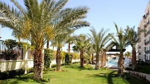 A well-maintained garden with palm trees, a swimming pool, and a building with balconies.