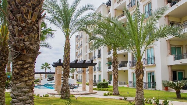 A resort with multiple-story buildings, palm trees, and a pool area.