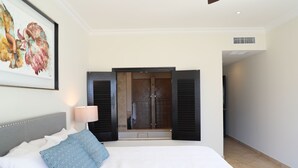 A hotel room with a large bed, a framed artwork on the wall, and a view of a shower area through open shutters.