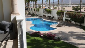 A swimming pool with a curved edge, surrounded by palm trees and a grassy area with flowers.