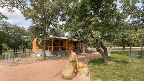 A rustic cabin with a wooden exterior, surrounded by a fenced area with trees and a clear sky. - Bakery Haus- Red Velvet Suite | Wonderful Porch (Fredericksburg)