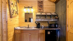 A compact kitchen with wooden cabinetry, a sink, a coffee maker, a microwave, and a refrigerator. - Bakery Haus- Red Velvet Suite | Wonderful Porch (Fredericksburg)