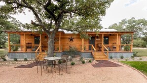 A wooden cabin with a porch, a dining table, and chairs. - Bakery Haus- Red Velvet Suite | Wonderful Porch (Fredericksburg)