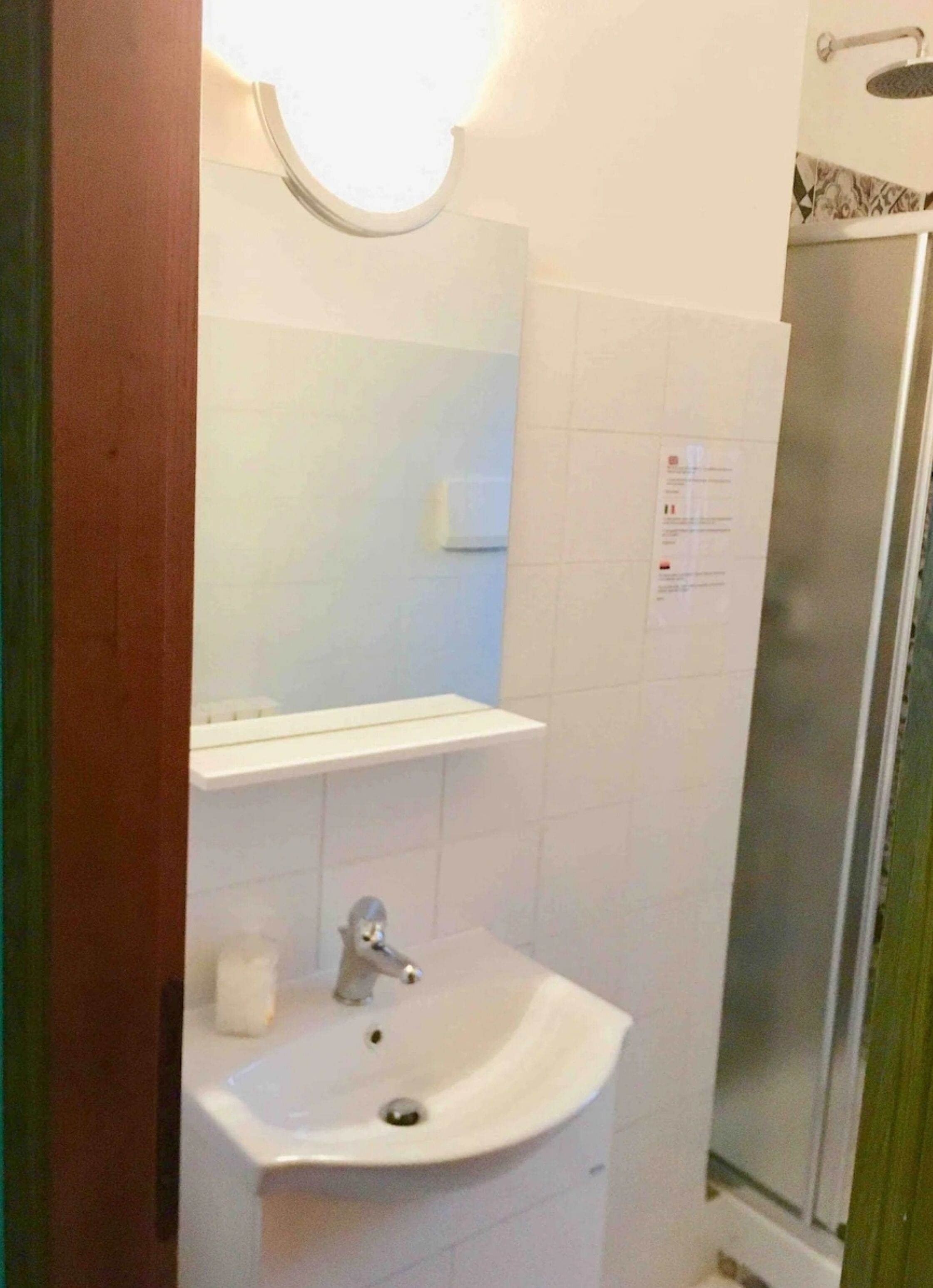 A bathroom with a white sink, a mirror with a light above it, and a shower area.