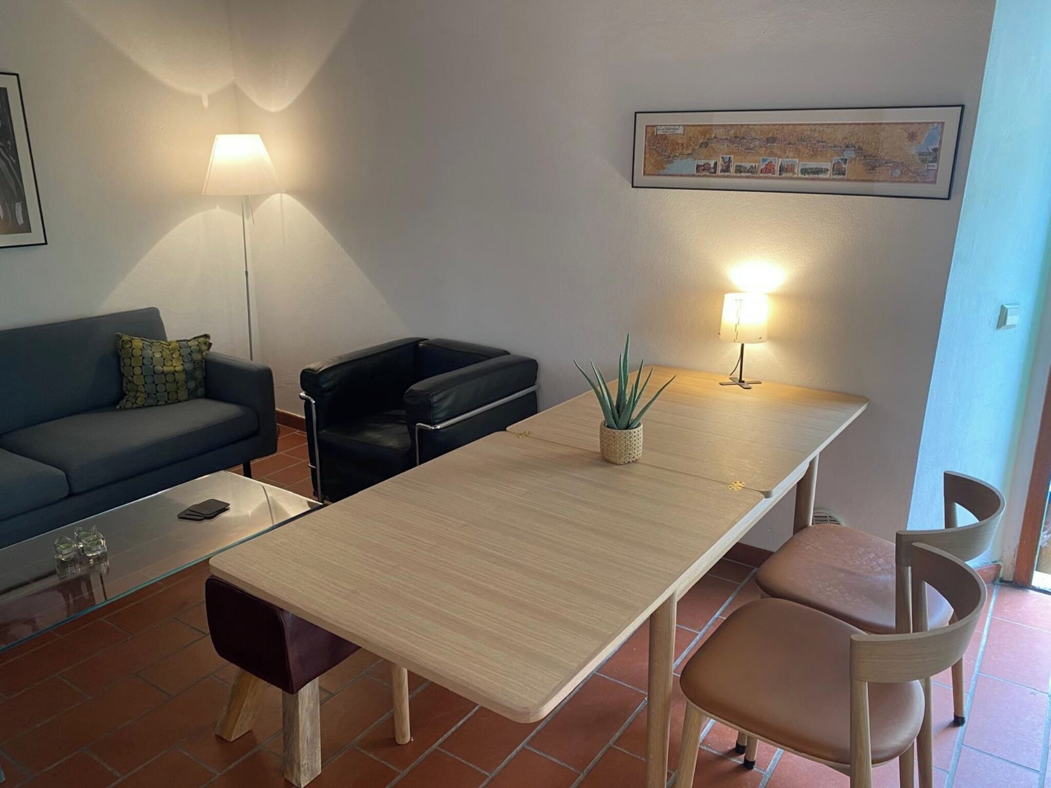 Un salon avec un canapé, un fauteuil en cuir noir, une table en bois et une plante en pot.