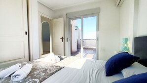 Hotellihuone, jossa on sänky, ikkunasta avautuva näkymä ulos ja ovi, joka johtaa parvekkeelle.