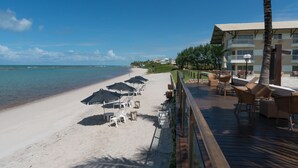 Un complexe hôtelier en bord de mer doté d’une terrasse en bois, de chaises longues et de parasols.