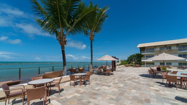 Une terrasse extérieure avec des tables et des chaises, des palmiers et une vue sur l’océan.