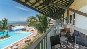 Un balcon avec vue sur une piscine et des palmiers, donnant sur l’océan.