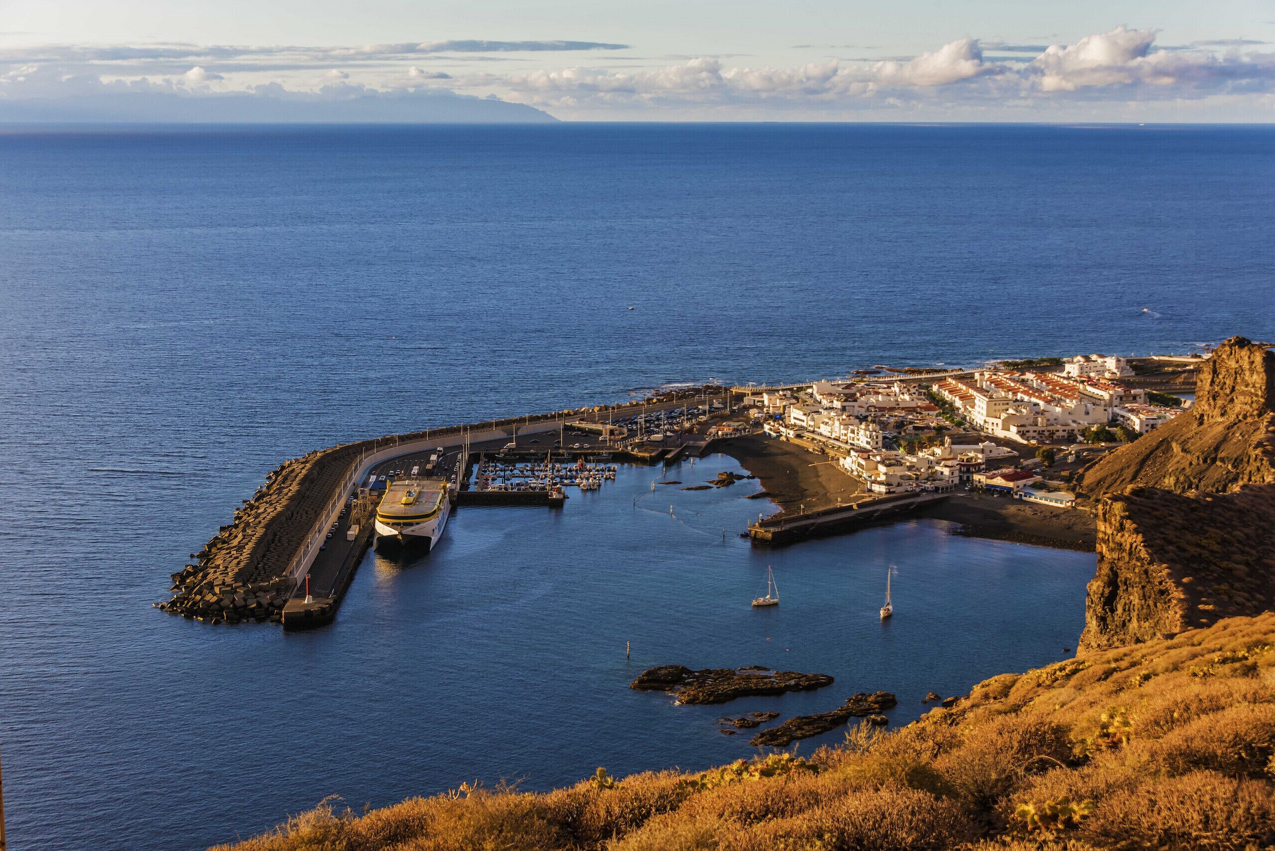 A coastal town with a marina, rocky terrain, and a clear view of the sea.
