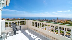 A balcony with a view of the sea, a chair, and a table.