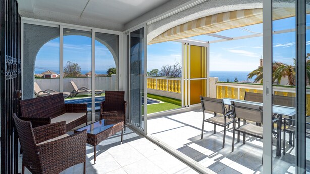 A balcony with wicker furniture, a glass door, and a view of the sea.