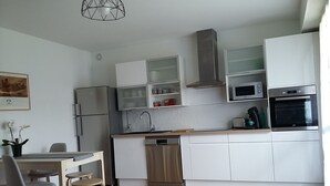 Ett modernt kök med vita skåp, rostfria vitvaror och en matplats med ett bord och stolar.