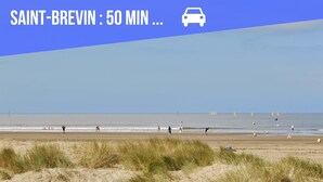 En strandscen med människor som promenerar och leker, en bilikon och text som anger att det är 50 minuter till Saint-Brevin.
