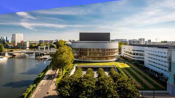A modern building with a curved facade, a river in the foreground, and a bridge in the background.