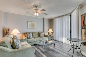 A living room with a sofa set, a coffee table, a glass-top table, a ceiling fan, and a painting on the wall.