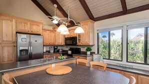 Una cocina con armarios de madera, encimeras de granito, refrigerador de acero inoxidable, microondas e isla grande con tabla de cortar.