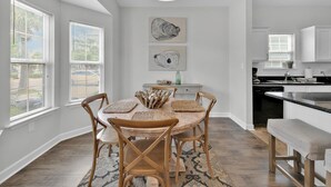 A dining area with a round table, four wooden chairs, and a woven placemat. There are two wall-mounted artworks above the table. - Luna Sea-Walk to Beach-Seaside-Community Pool (Santa Rosa Beach)