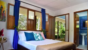 A bedroom with a bed, curtains, a nightstand, a painting, and a view of the outdoors. - Playa Mareygua (Santa Marta)