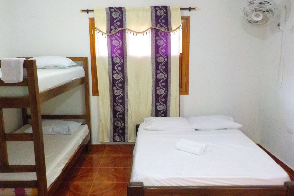 A room with a bunk bed, a single bed, and a curtain with a floral pattern.