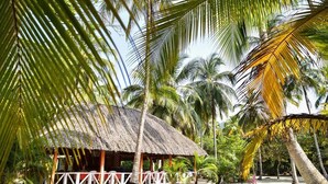 A thatched-roof hut with a white railing, surrounded by palm trees and greenery. - Playa Mareygua (Santa Marta)