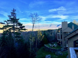 A house with a stone patio and outdoor seating, surrounded by trees and mountains in the background.