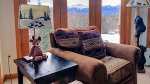 Una habitación acogedora con un sillón marrón, una mesita con un osito de peluche y una lámpara con motivos de oso.