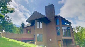 Una casa de dos pisos con techo inclinado, ventanas grandes y chimenea.